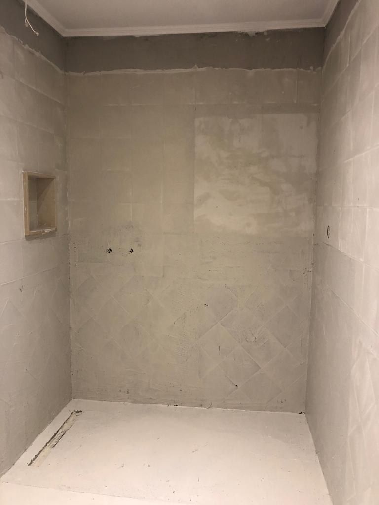 Microcement base coats being applied across the shower walls, niche and floor